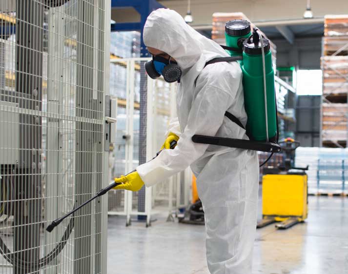 Person hält Sprühgerät an Zaun in Industriehalle