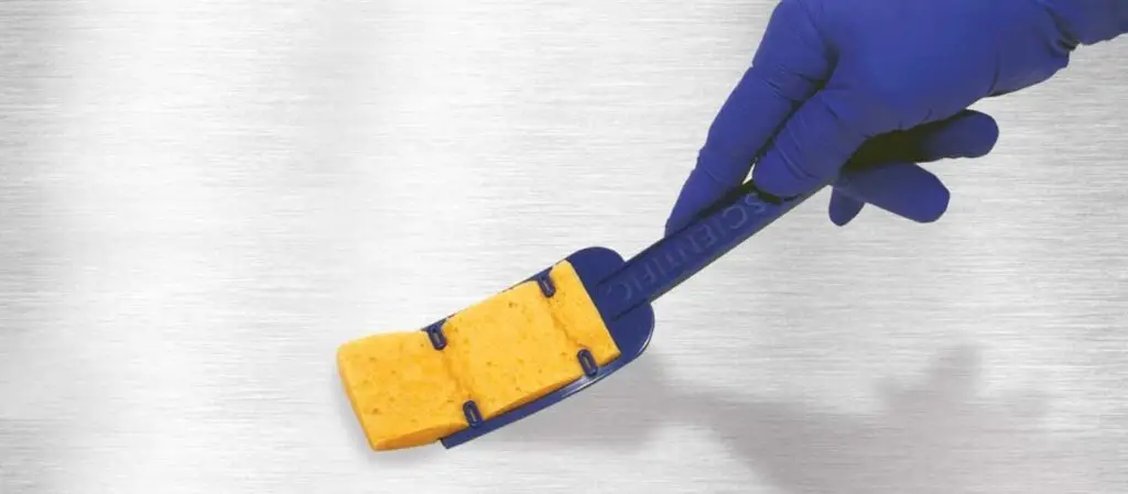 Hand in Gummihandschuh hält Schwamm an Stiel an eine Oberfläche