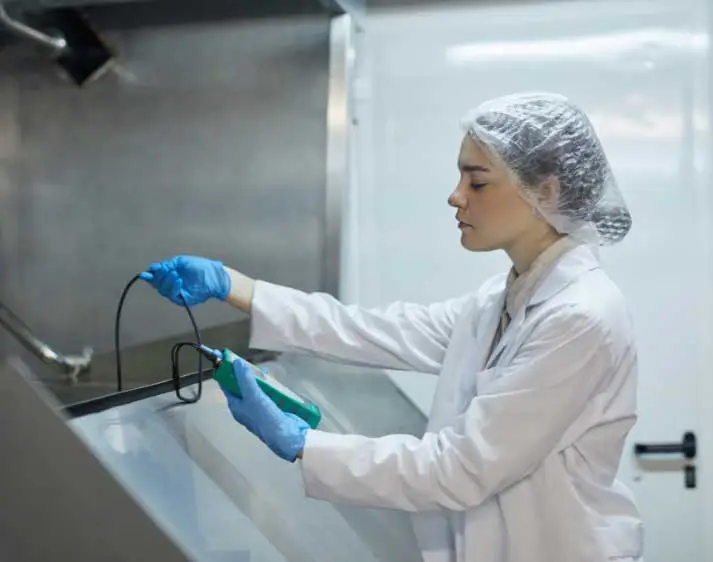 Frau mit Haarnetz und Gummihandschuhen hält Gerät in der Hand