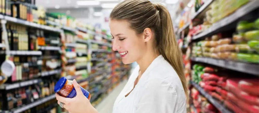 Frau schaut Etikett von Sauce im Glas an, im Supermarkt