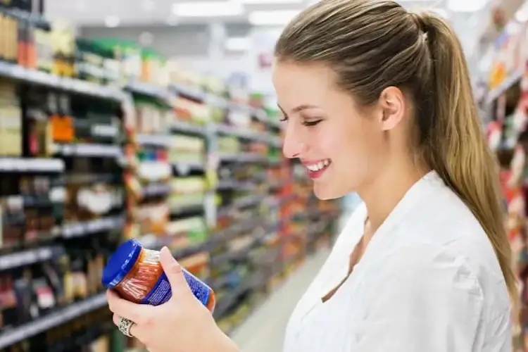 Frau schaut Etikett von Sauce im Glas an, im Supermarkt.