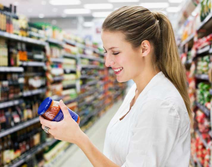 Frau schaut Etikett von Sauce im Glas an, im Supermarkt