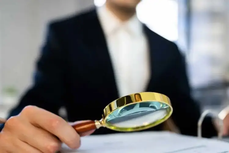 Person in Businesskleidung hält Lupe auf Ordner.