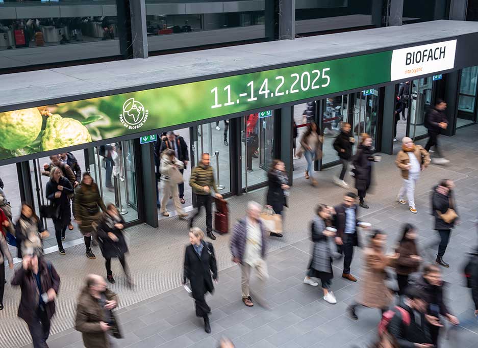 Menschen unterwegs in Halle vor unter Schild von Biofachmesse 2025