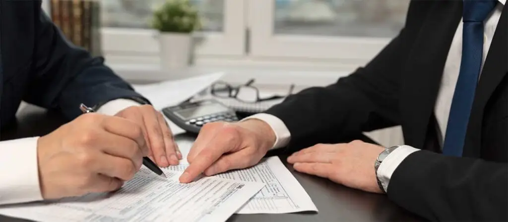 Hände zweier Personen über Papiere mit Formularen oder Verträgen