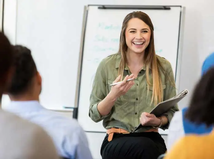 Frau mit Klemmbrett, lachend, vor Flipchart stehend, ihr Blick richtet sich auf Publikum