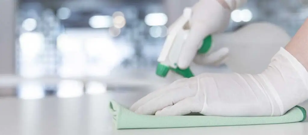 Hände in Gummihandschuhen reinigen Fläche mir Sprühflasche und Lappen
