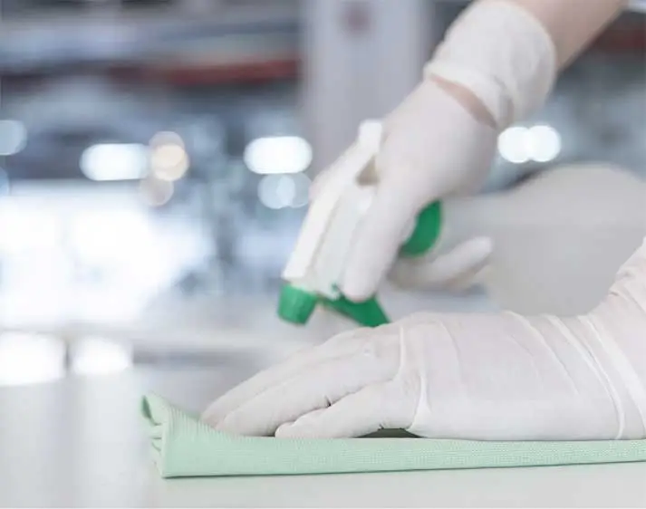 Hände in Gummihandschuhen reinigen Fläche mir Sprühflasche und Lappen