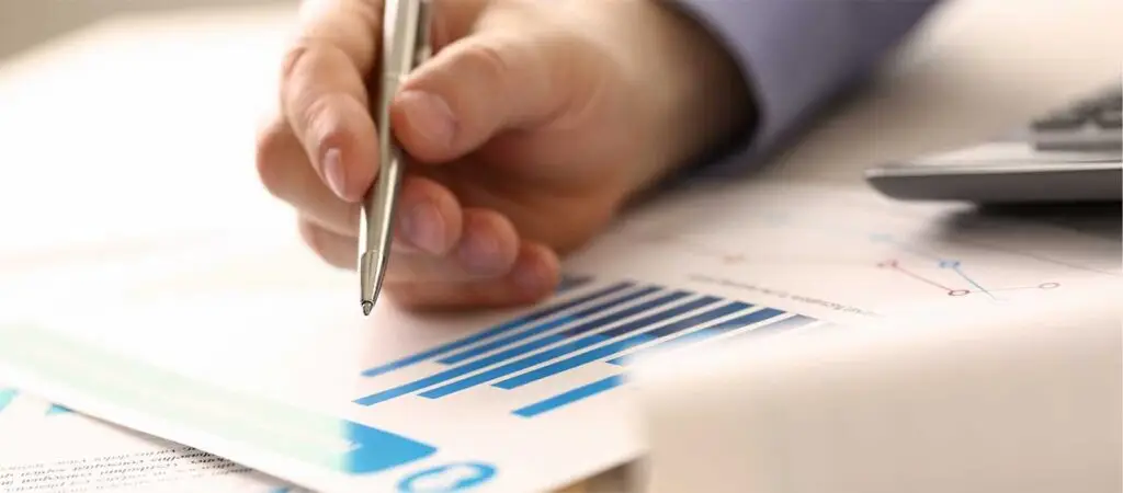 Hand hält Kugelschreiber über Unterlagen mit Diagrammen darauf