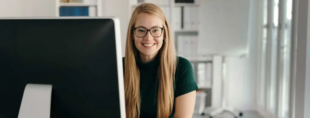 Frau lächelnd hinter Cumputerbildschirm am Schreibtisch