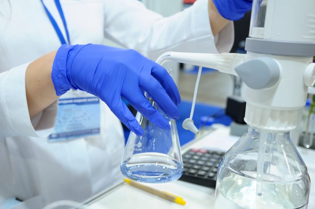 Lab assistant’s hands in blue gloves adjusting the titrator to measure quality of drinking water.