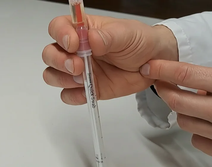 A laboratory person's hands holding a Quick Swab.