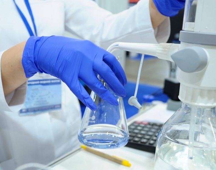 Lab assistant’s hands in blue gloves adjusting the titrator to measure quality of drinking water.