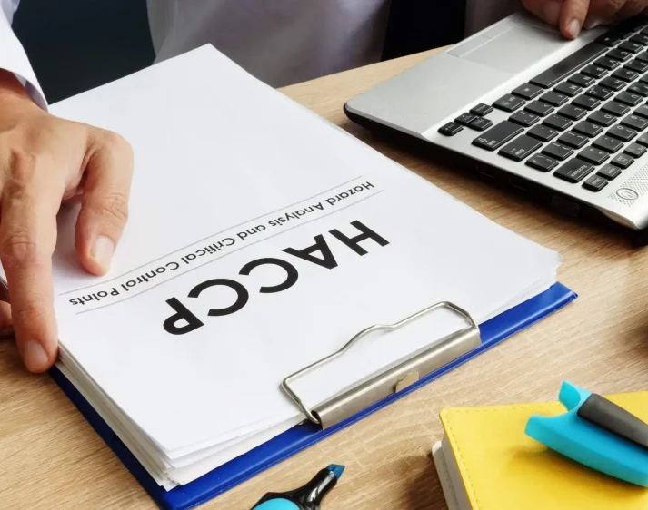 A hand holding clipboard holding papers titled "HACCP".